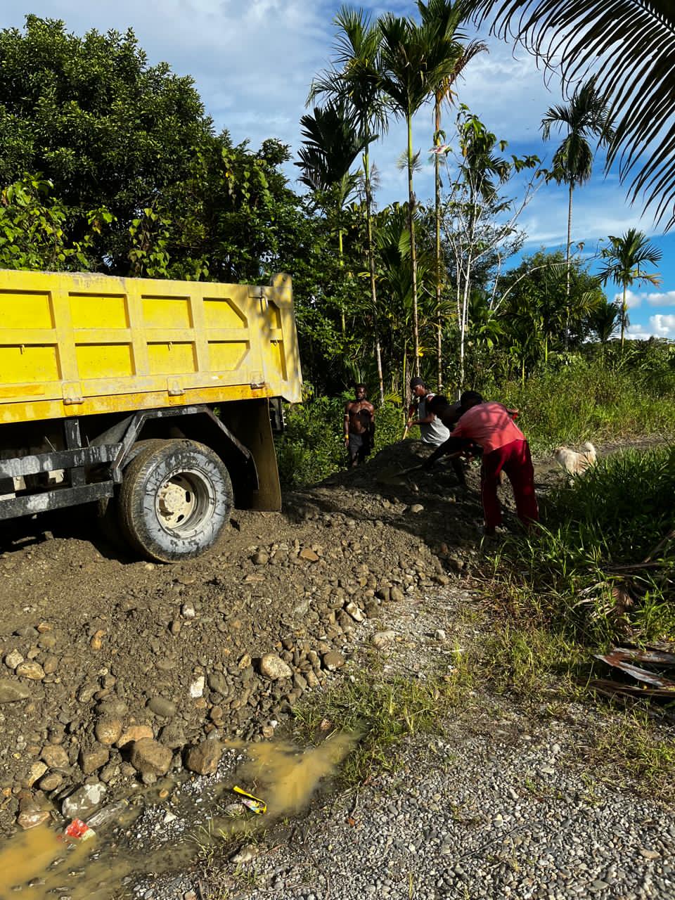 Truk pengangkut material saat menumpahkan material kemudian warga yang merapikan material tersebut